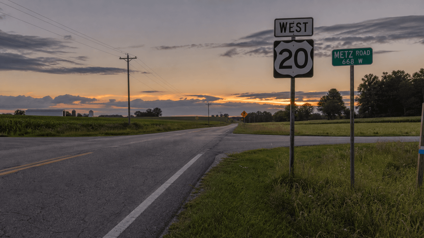 Rural intersection of U.S. 20 and Metz Road east of Angola in Steuben County, Indiana at dusk, near the scene of a fatal Fourth-of-July pontoon-trailer crash.