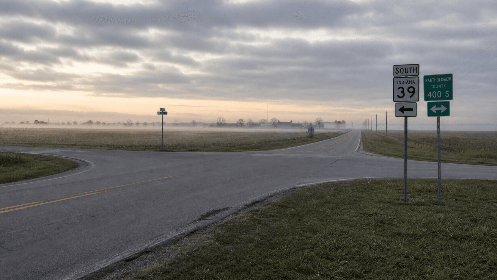 Rural Indiana two-lane state highway intersection at dawn with weathered route signs and flat farmland in the background, representing the SR-1 and County Road 400 South junction in southwest Jay County where a fatal failure-to-yield crash occurred July 14, 2026