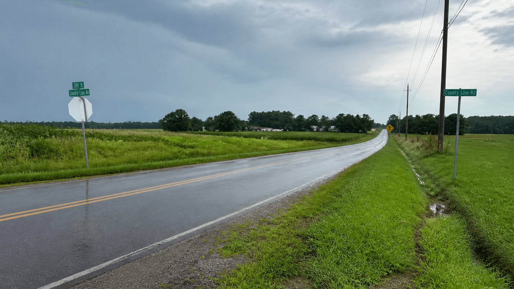 Wet rural county-road intersection in DeKalb County, Indiana, representing the hydroplaning crash near County Road 12 and County Road 39.