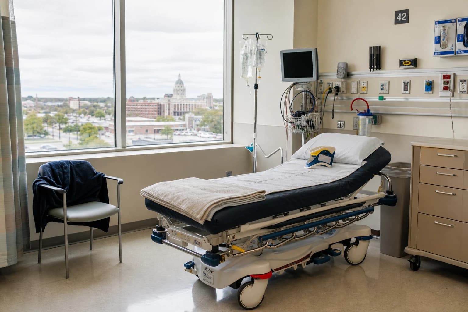 Empty Fort Wayne hospital ER bay set up for a rideshare-crash passenger with a wheeled stretcher, IV pole, cervical collar, and folded jacket — the medical timeline a Fort Wayne Uber and Lyft accident attorney builds every passenger case on