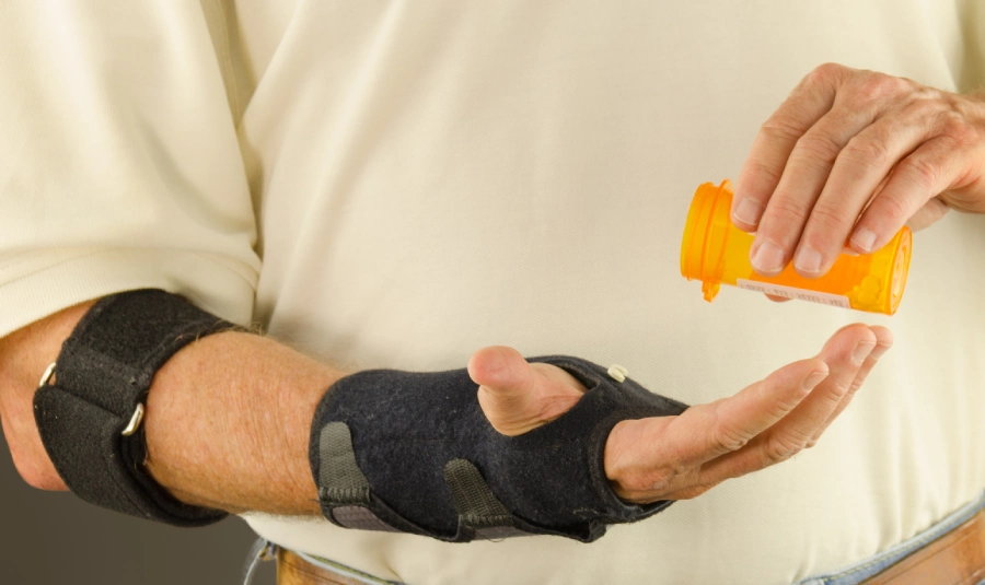 A man wearing a wrist brace pours prescription pills into his hand.