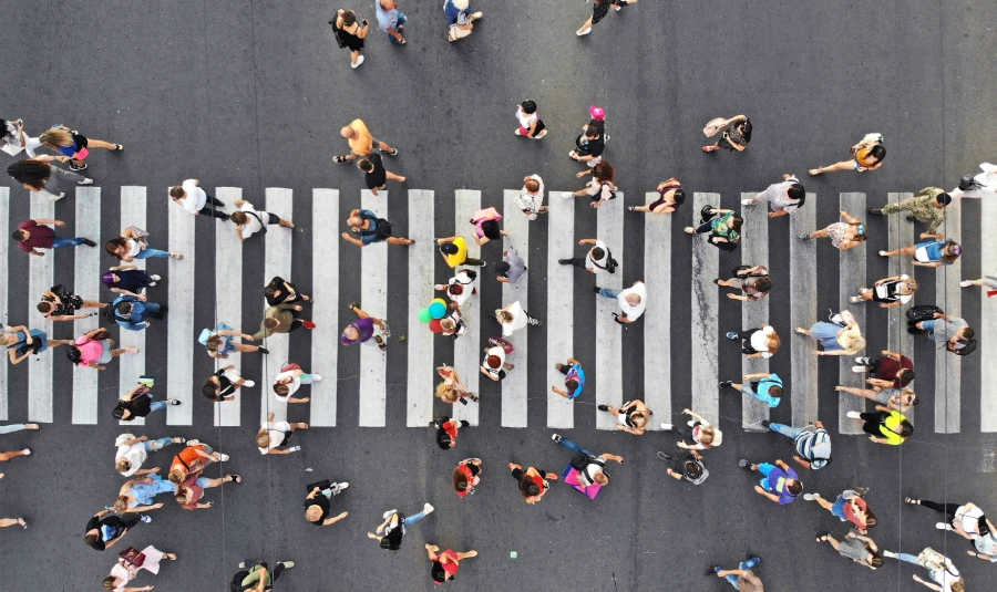 Many people cross on and around a large crosswalk.