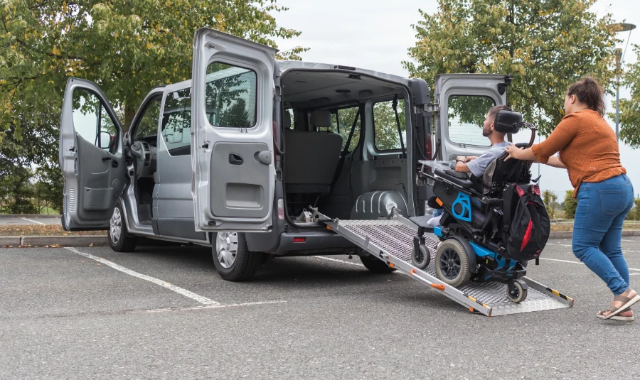 A woman pushes a disabled man in a wheelchair into a handicap-accessible van.