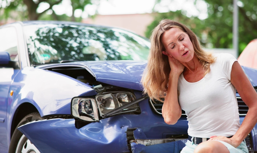 Woman holds her neck in front of her vehicle after a car accident