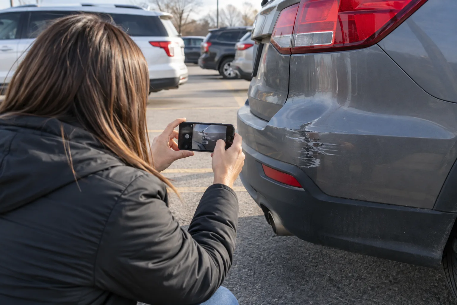 Person photographing vehicle damage in a Fort Wayne parking area