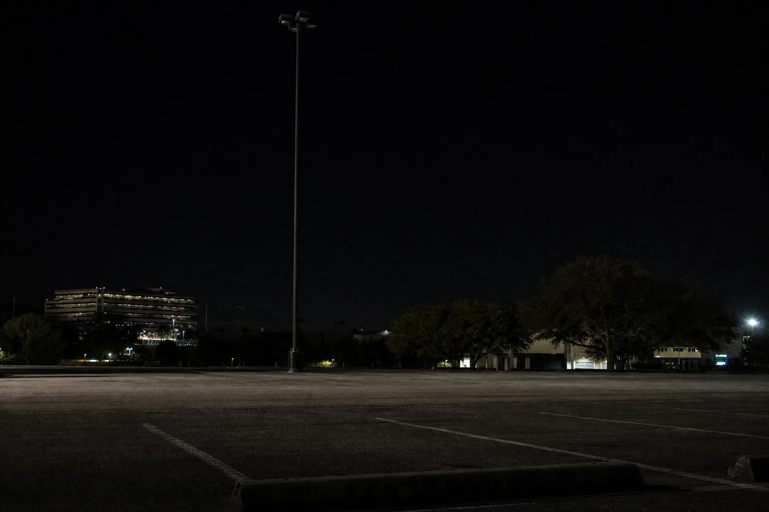Dark parking lot with an unlit pole light and a barely visible curb stop