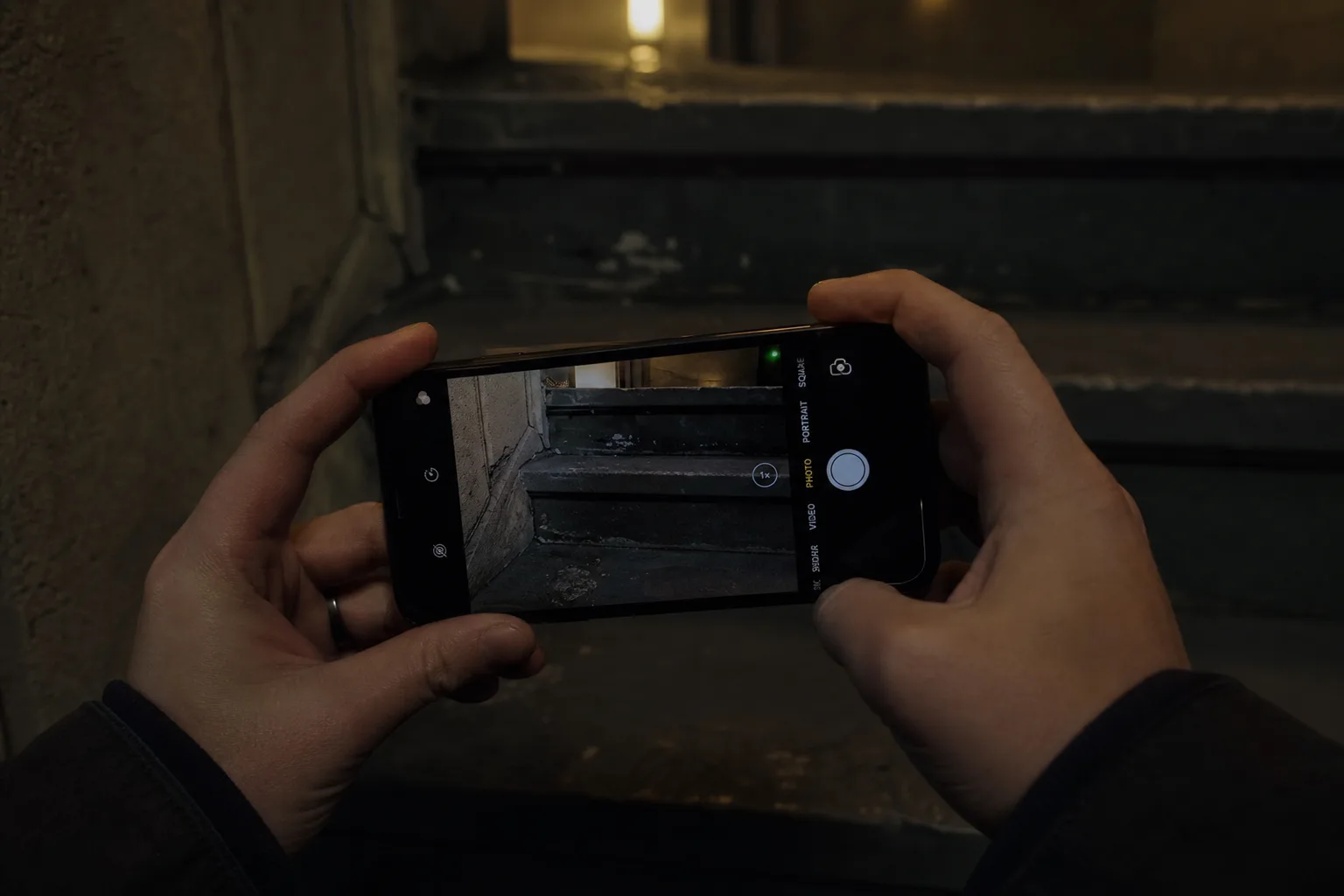 Person photographing a dark stairway step in low light with a smartphone