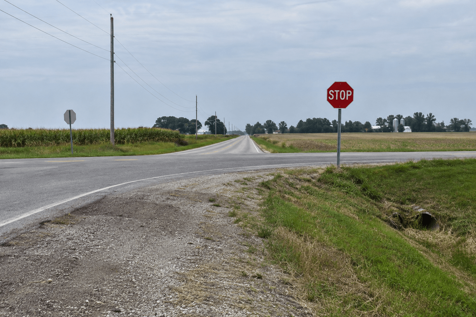 Rural stop-sign intersection and roadside drainage ditch representing the County Road 9 rollover location in Elkhart County.
