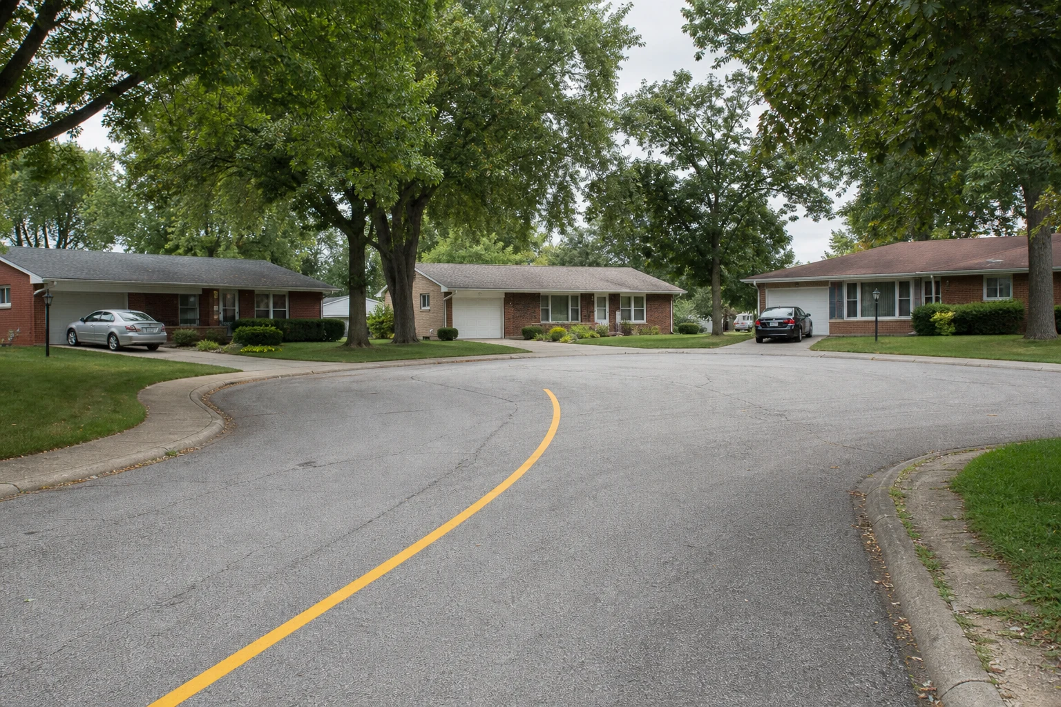 Fort Wayne suburban cul-de-sac with ranch-style homes around the loop, mature oak trees, and freshly painted yellow center line — the residential streets where most Allen County Amazon delivery accidents happen and where the evidence preservation begins.