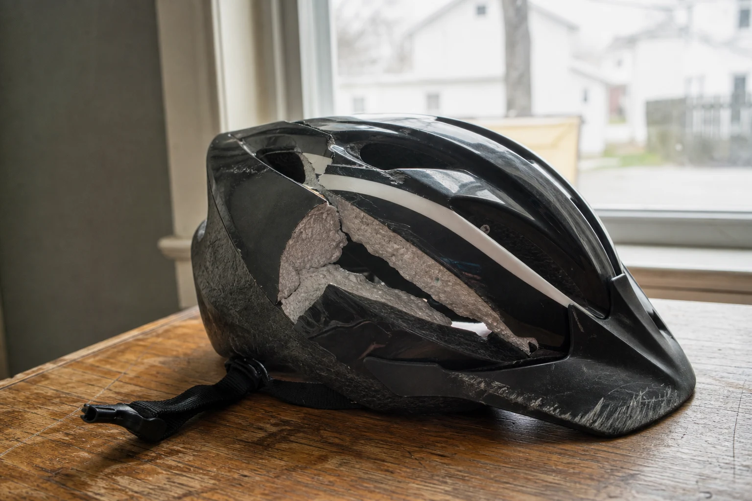 Road-bike helmet with a visible compression crack through the polystyrene shell, scuffed paint, scrape pattern on the visor — physical evidence of head impact a Fort Wayne bicycle accident lawyer documents