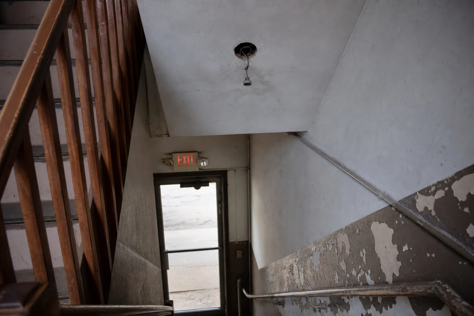 Dimly lit Fort Wayne apartment-building stairwell with a burned-out overhead light fixture and faint emergency lighting at the bottom — the kind of inadequate-lighting negligence an Indiana negligence attorney litigates