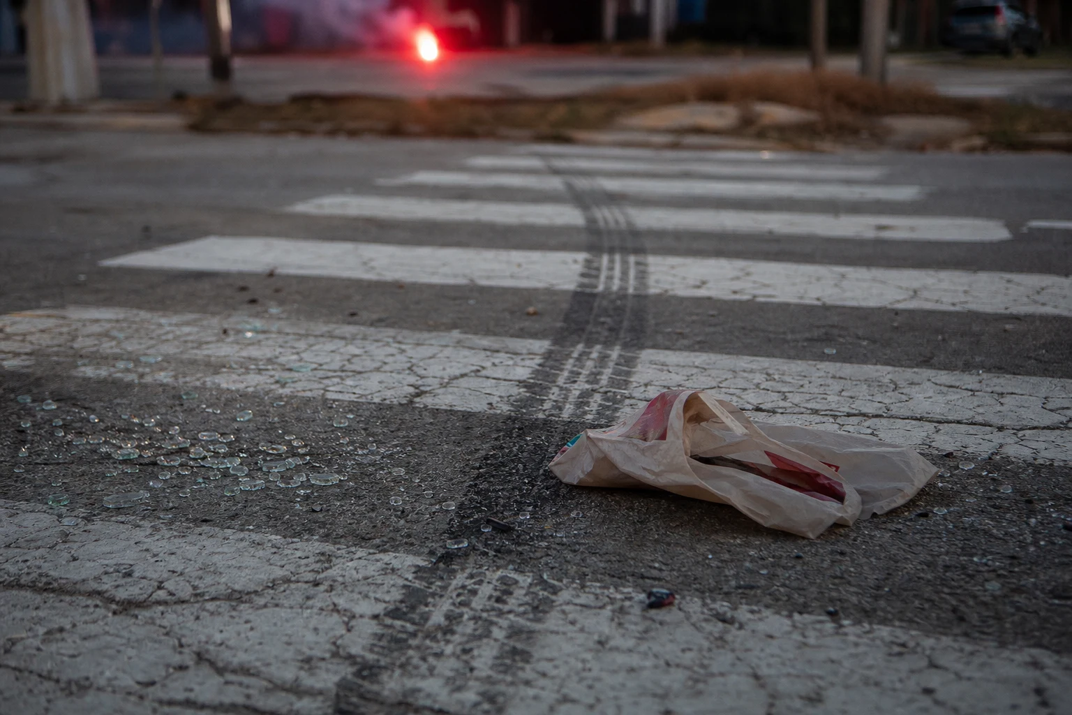 Fort Wayne crosswalk on asphalt with a single skid mark crossing the white striped paint, a dropped shopping bag, broken safety glass, dusk lighting — the scene a Fort Wayne pedestrian accident attorney preserves immediately
