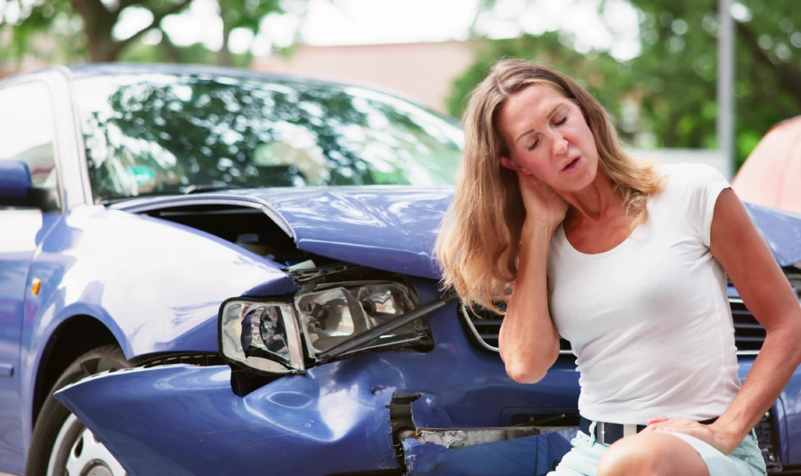 Woman holds her neck in front of her vehicle after a car accident