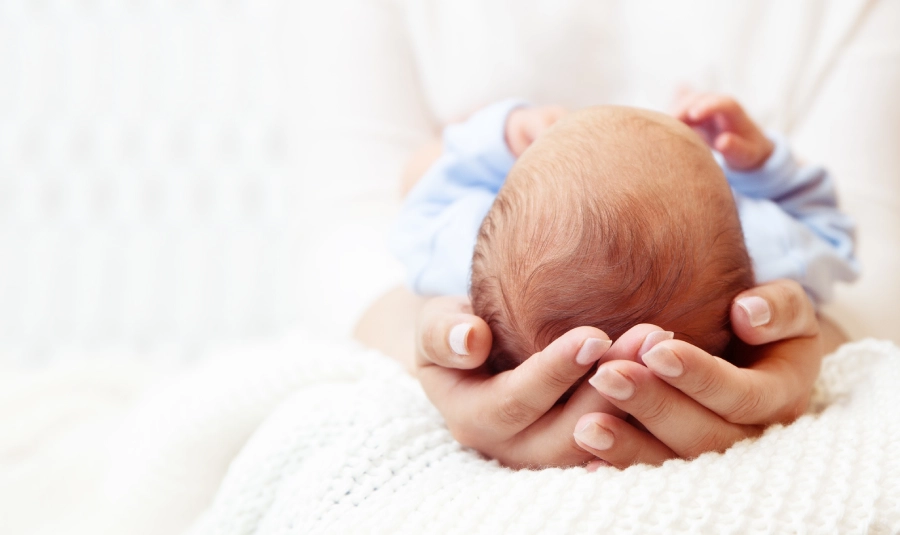 A woman holds a small baby in her lap with its head in her hands.