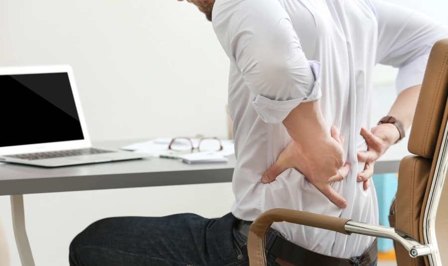 A man holds his lower back in pain at his desk.