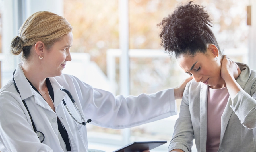 A woman holds her neck as a doctor attends to her.