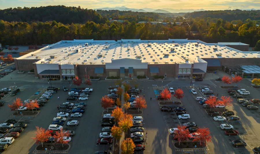 A large warehouse with many cars parked in the parking lot in front of it.